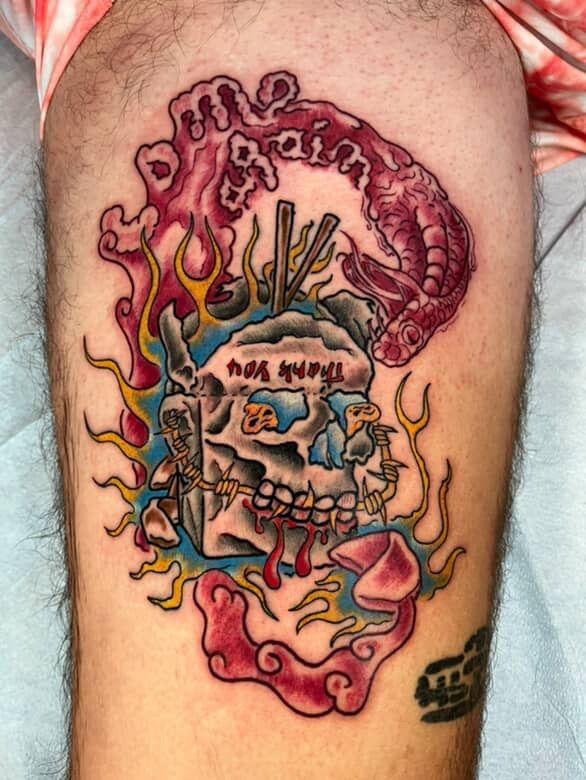 Tattoo of a skull with noodles, chopsticks, and flames; a person's leg.