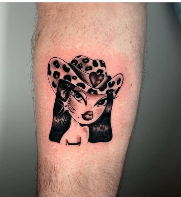 Bratz-style portrait tattoo, wearing a leopard print cowboy hat. Black and white ink on arm.