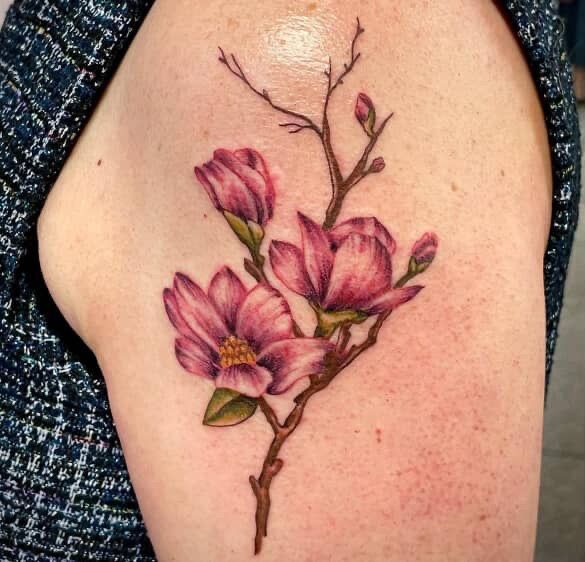 Tattoo of pink magnolia flowers on a person's upper arm.