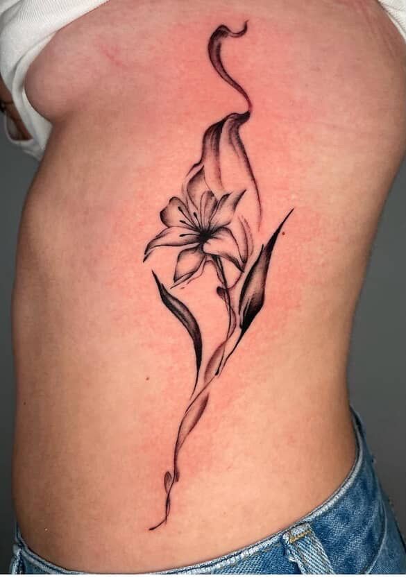Black and gray lily tattoo on a person's side, with flowing lines and leaf detail.