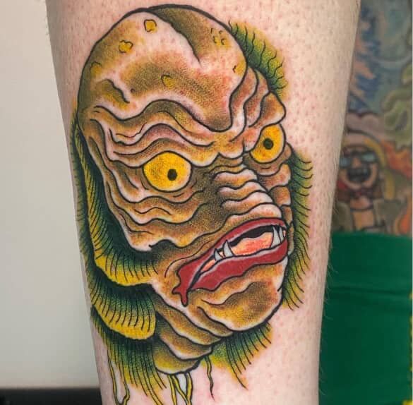 Creature from the Black Lagoon tattoo on leg. Yellow eyes, green gills, brown skin, red mouth.