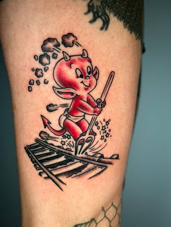 Red devil character tattoo skiing on a railroad track, with steam.