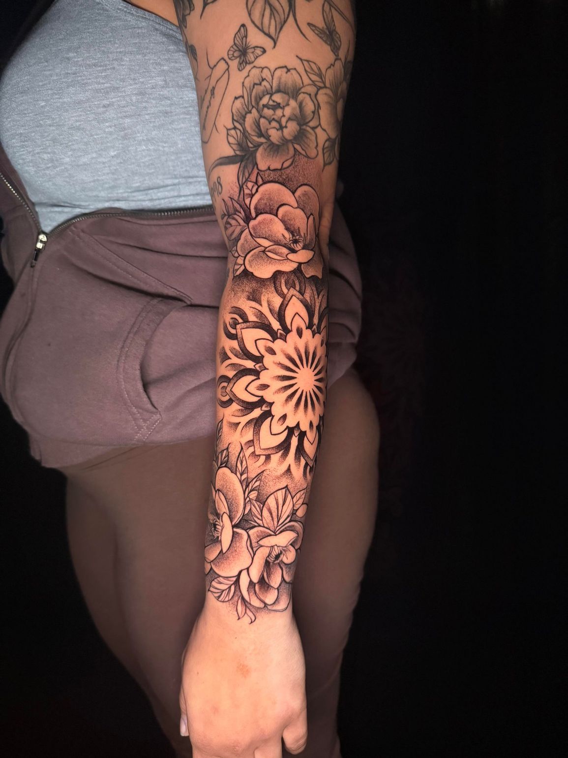 Arm covered in black floral tattoo sleeve next to a gray top and brown shorts.