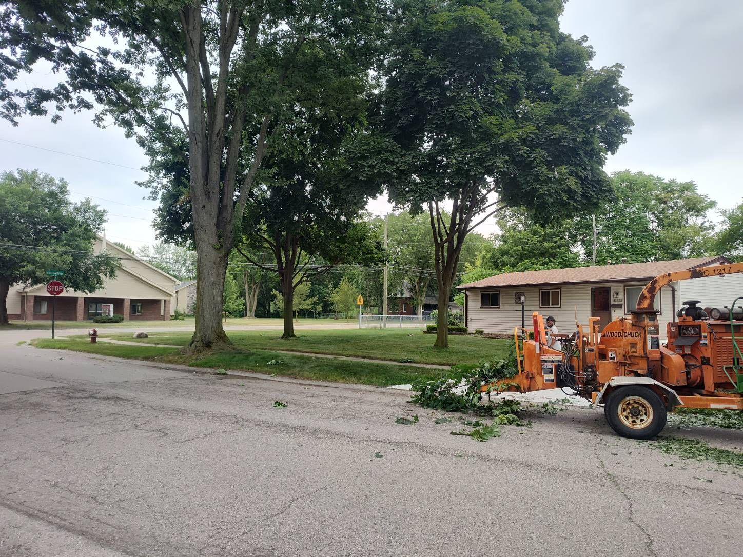 A tree chipper is parked on the side of the road in front of a house.