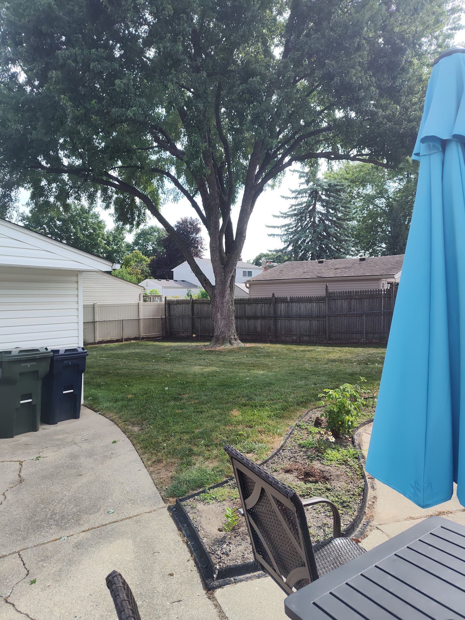 A backyard with a blue umbrella and a table and chairs