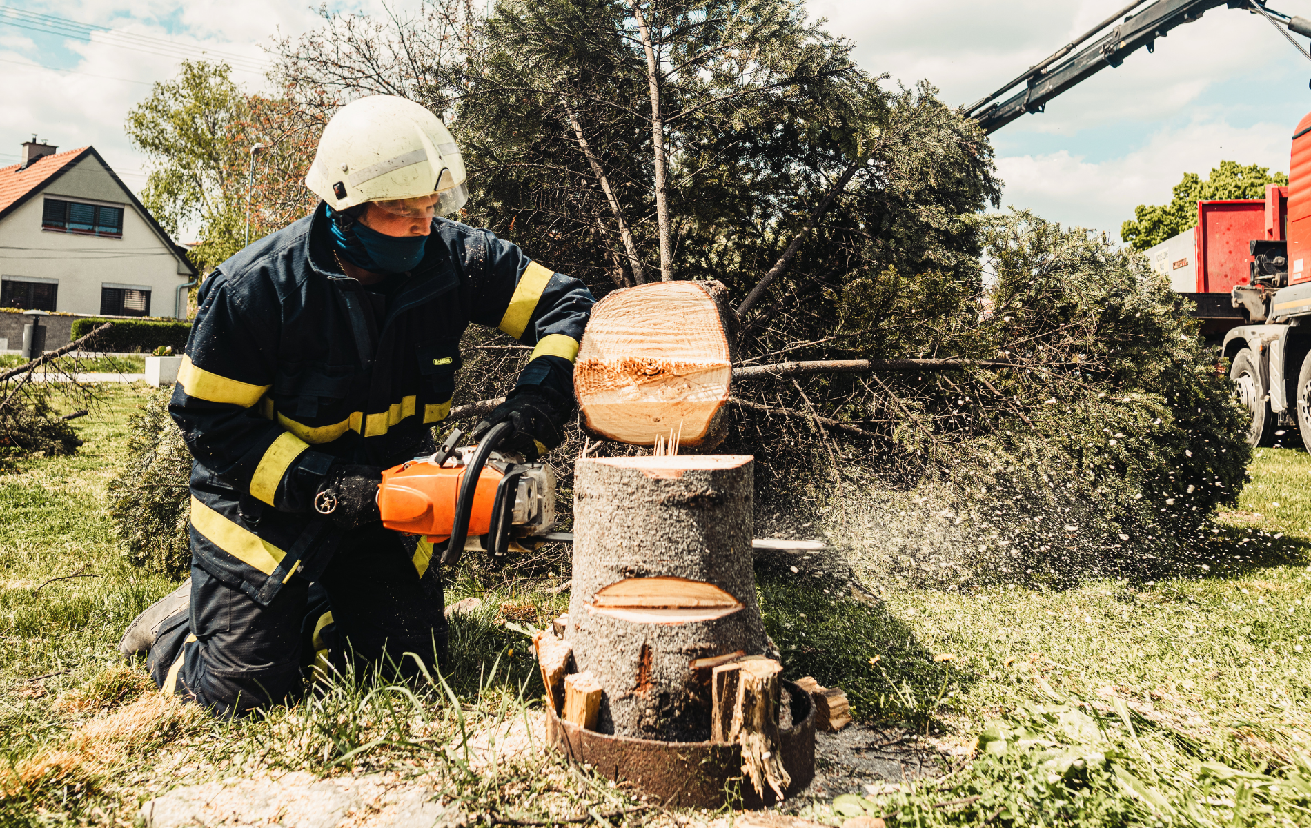 A fireman is cutting a tree stump with a chainsaw.