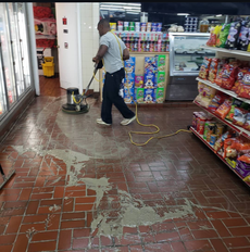 Person using a floor buffer to clean a grocery store floor, with shelves of products visible.