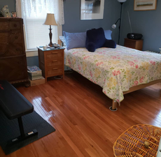 Bedroom with bed, nightstand, dresser, weight bench, and wood floor.