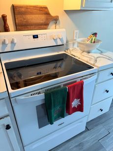 White electric stove with open stovetop and two Christmas-themed towels hanging on the handle.