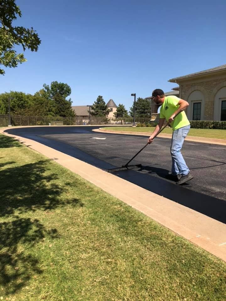 A man is applying asphalt to a parking lot with a broom.