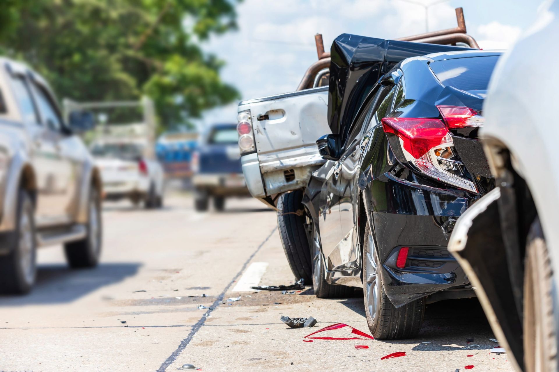 Damaged black sedan and white car after a roadside collision, with debris on the pavement.