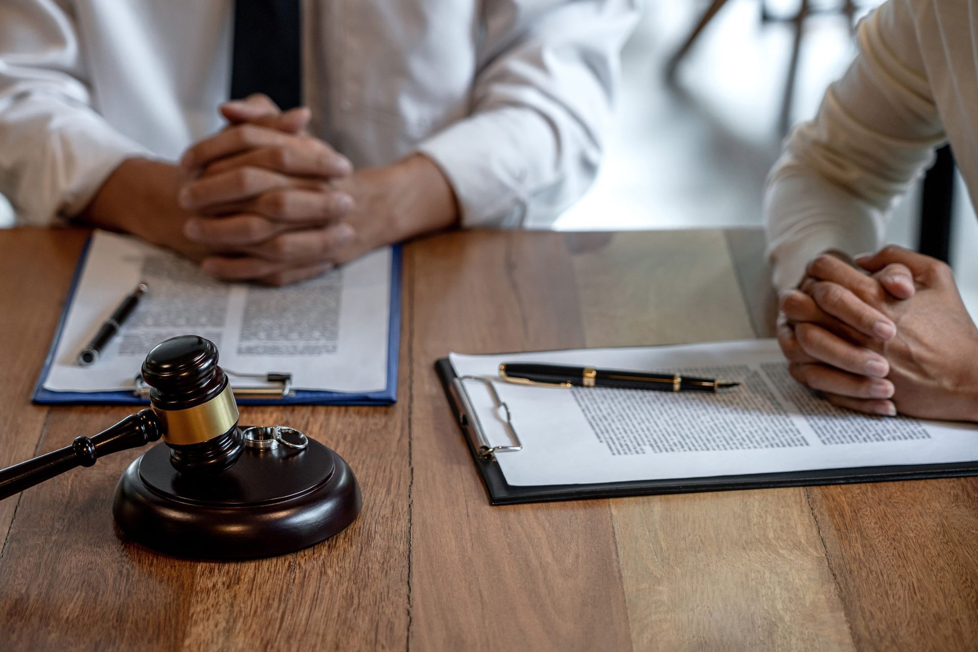 Courtroom gavel on a table beside two people’s clasped hands and documents on clipboards