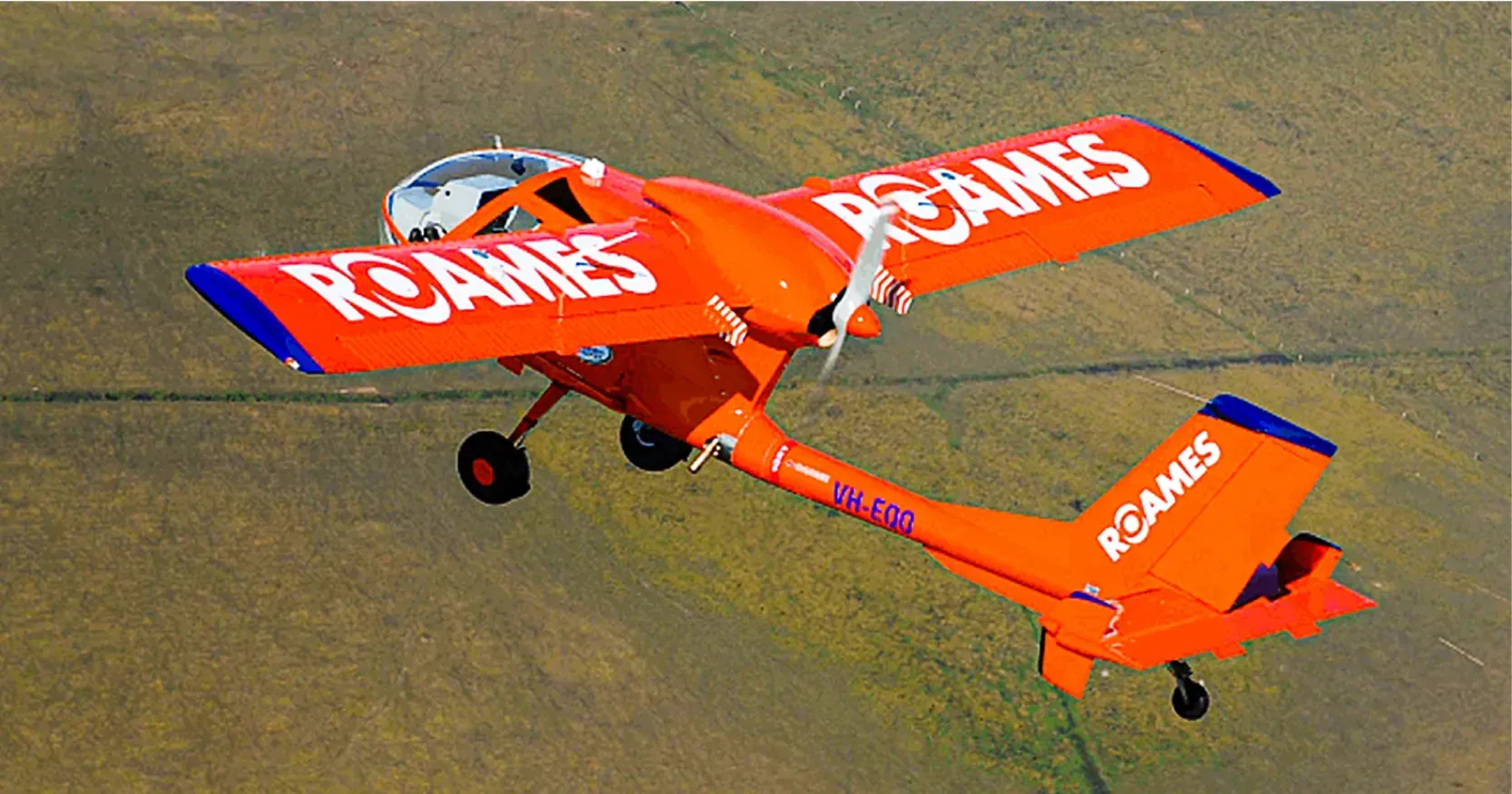 A ROAMES branded lidar orange airplane is flying over a field.