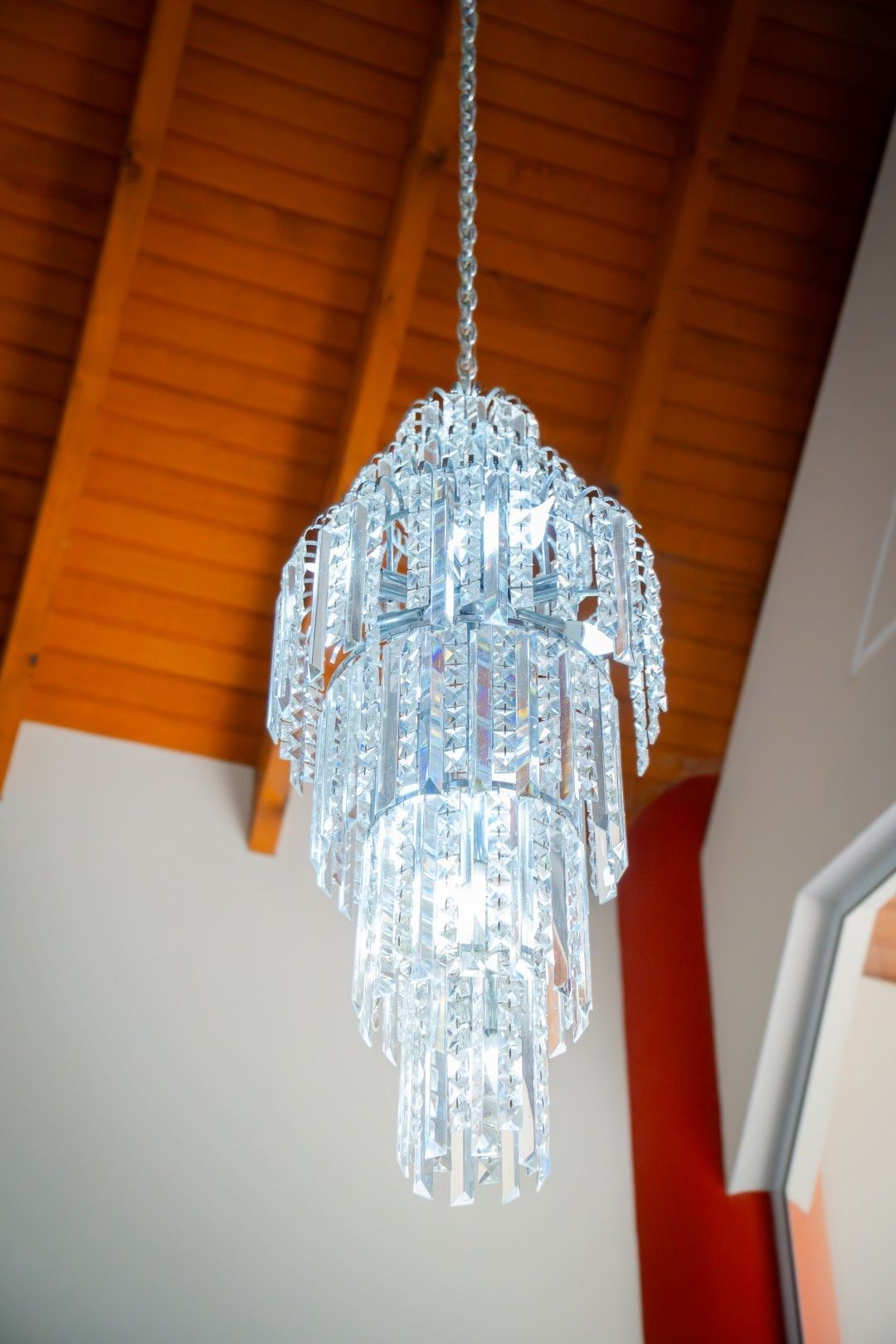 Um lustre de cristal pende de um teto de madeira; uma luminária ilumina o ambiente.