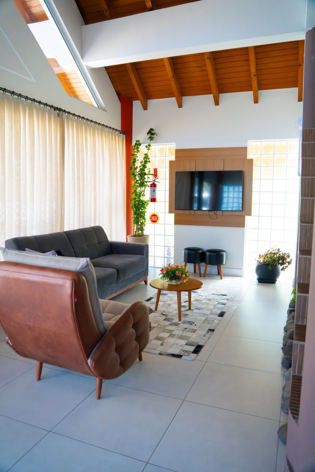 Sala de estar com sofá cinza, poltrona marrom, TV, tapete e luz natural.