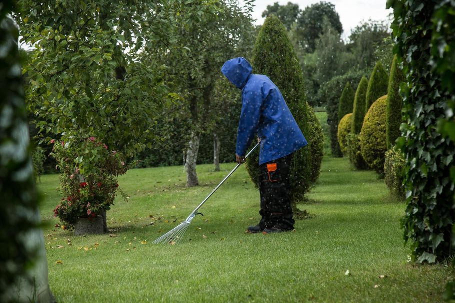 Person in blue raincoat mowing a green lawn in a garden during light rain