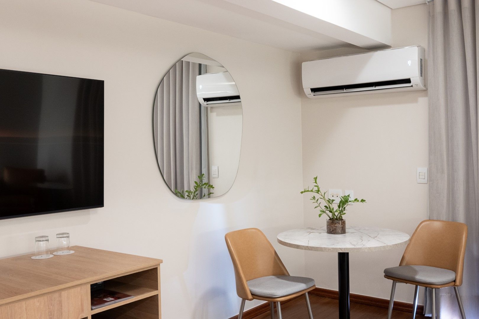 Uma sala de estar com mesa, cadeiras, televisão e ar condicionado.