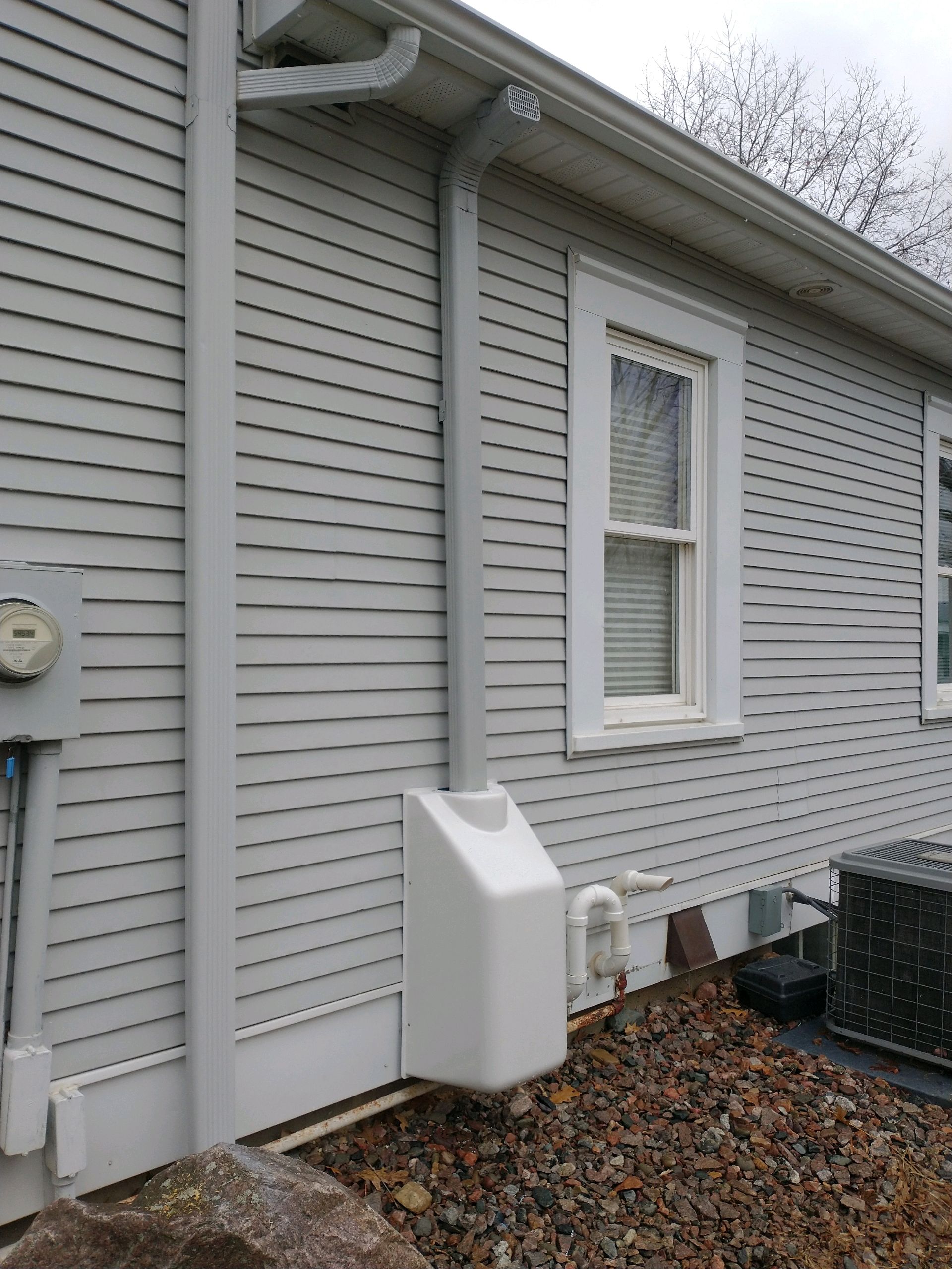 Light gray house exterior with white trim, window, gutter, and a white box-shaped utility item next to a window.