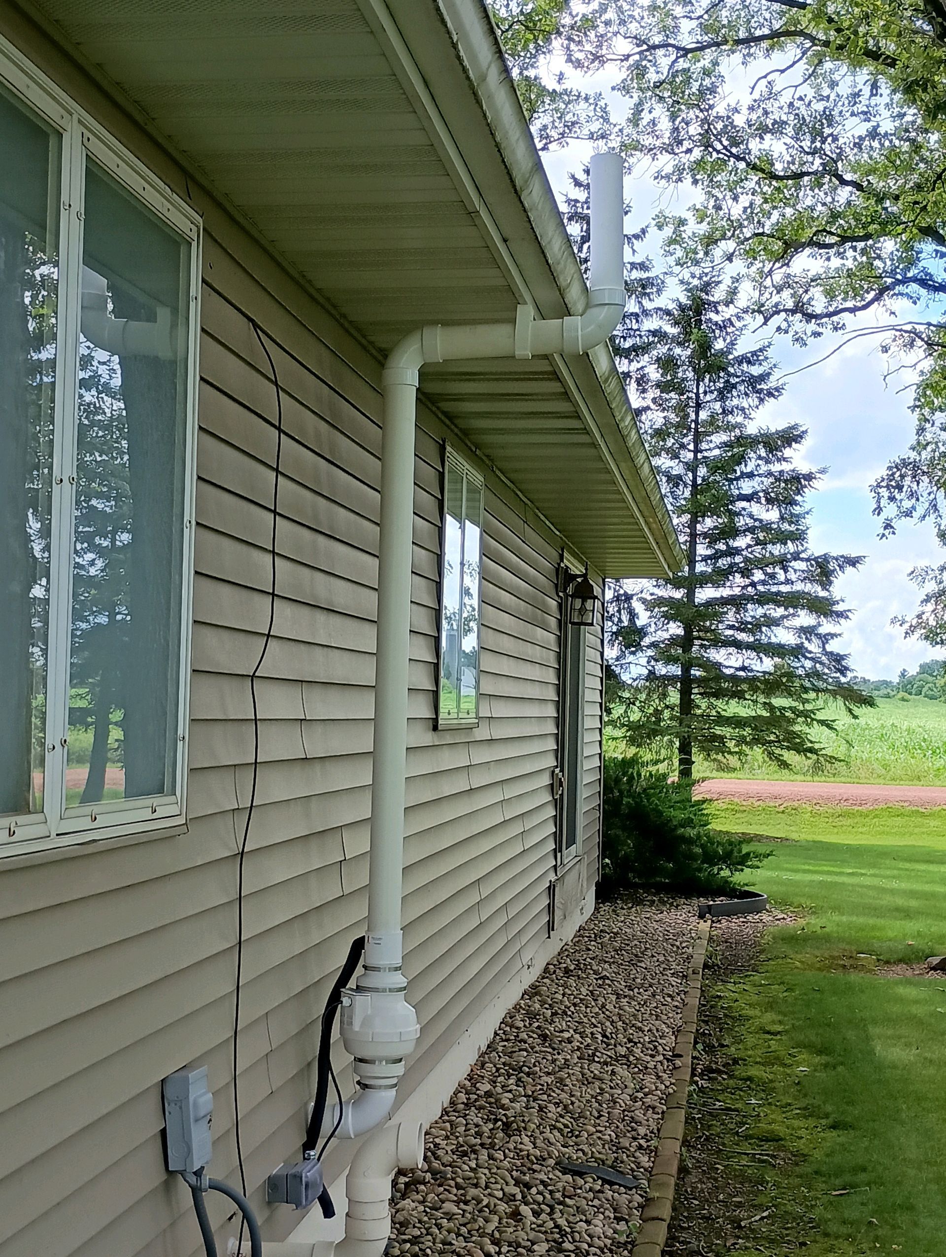White pipe extending from a house's roofline, running down the siding.