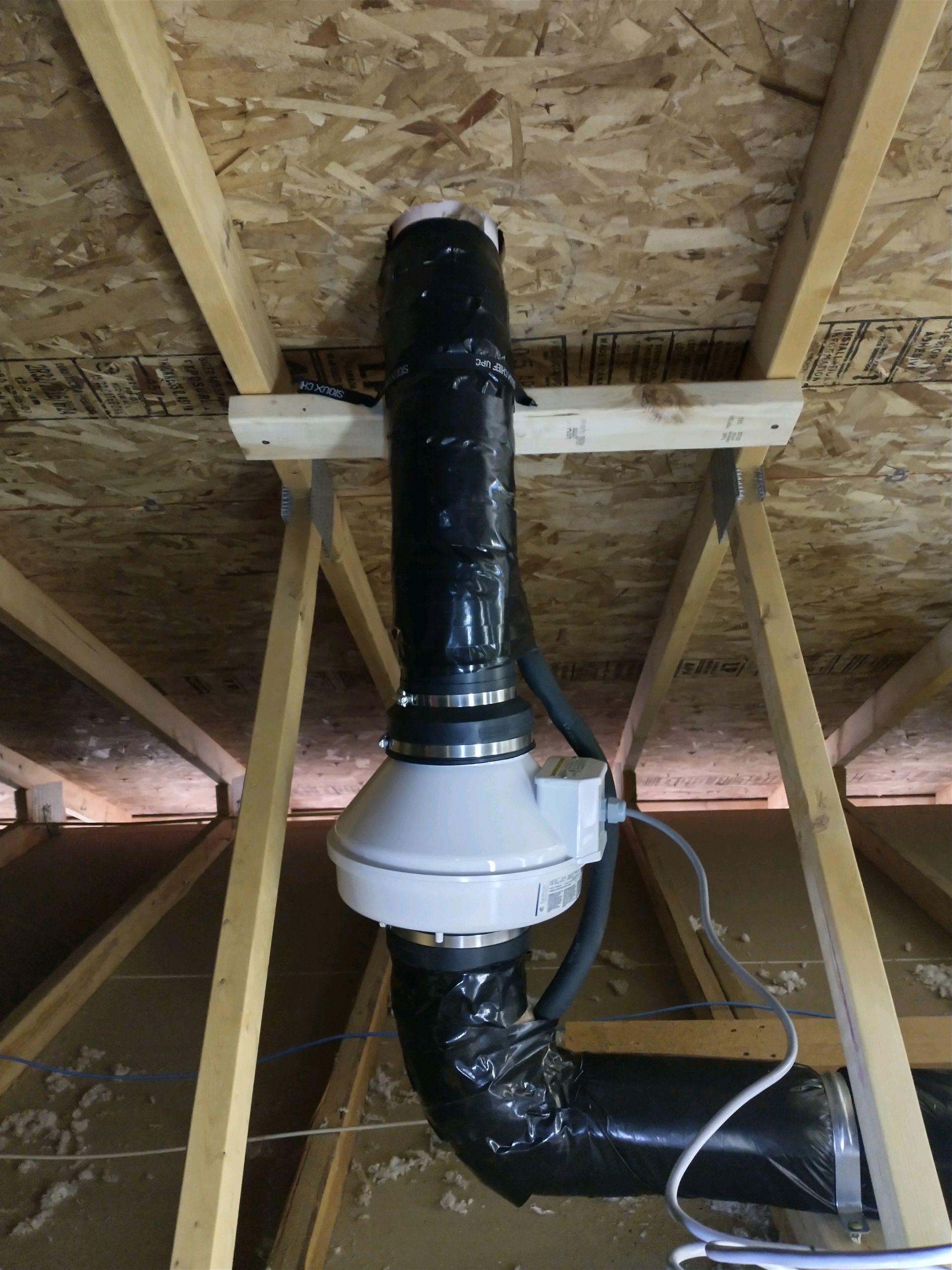 HVAC fan and ductwork installed in an attic. The fan is white, the ducting is black, and the supports are wood.