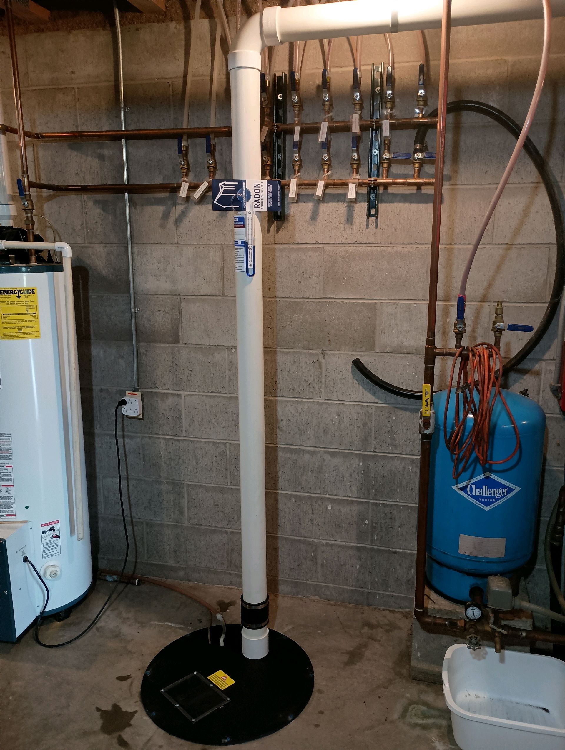 Basement with a sump pump, water heater, and water pressure tank against a cinder block wall.