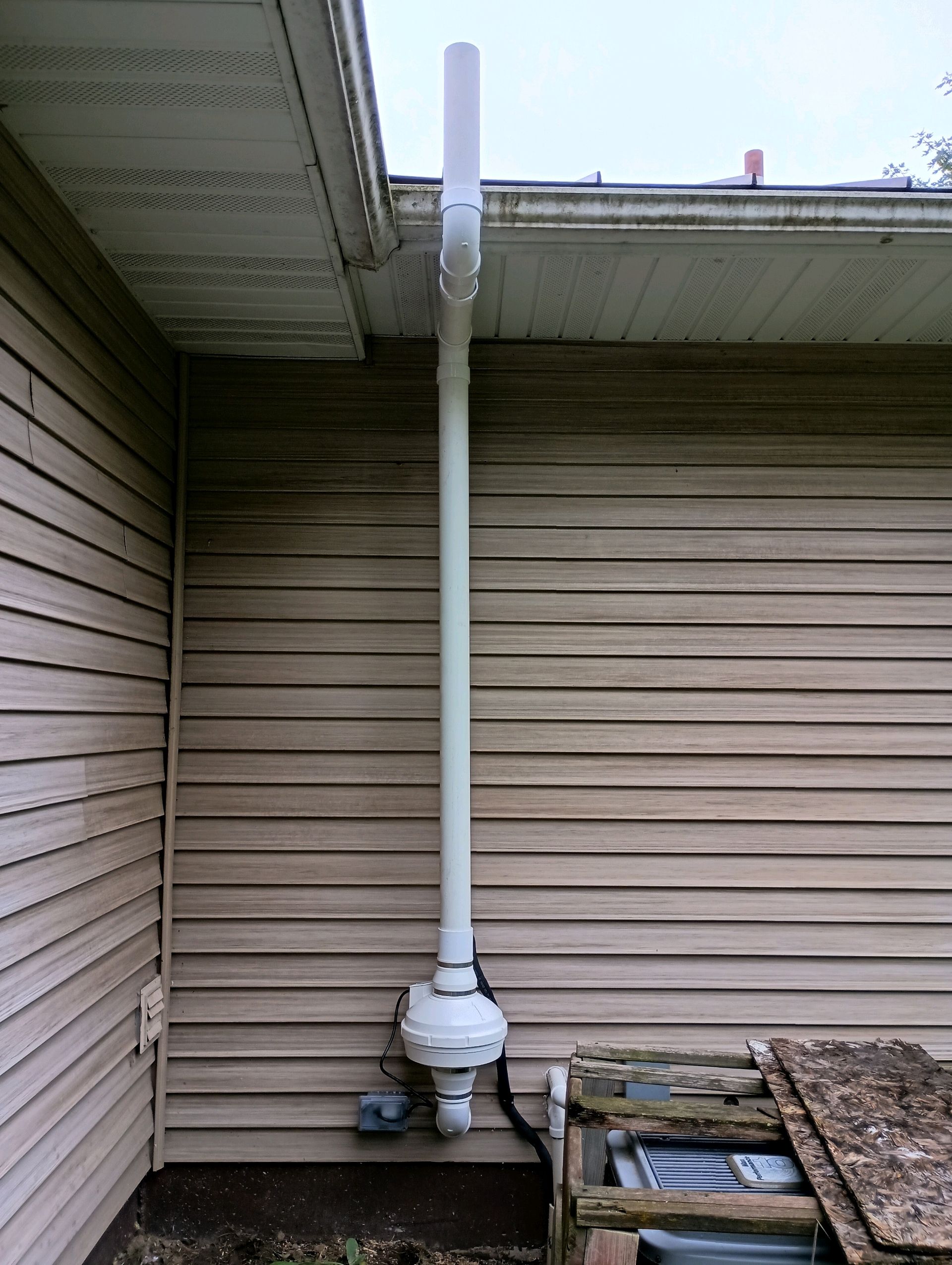 White PVC pipe downspout attached to a building's siding, with a curved section and a bulbous attachment near the ground.