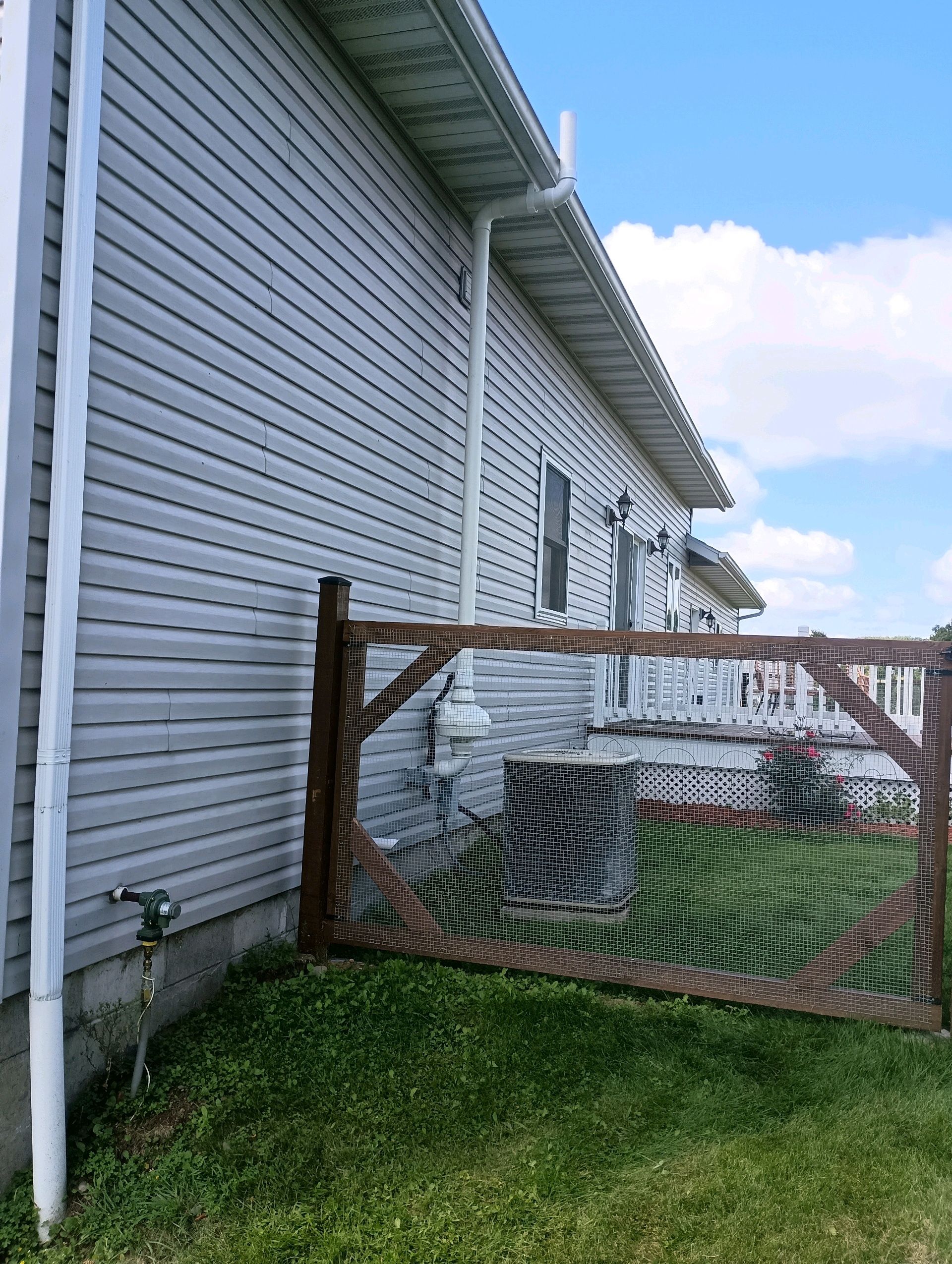 Side view of a white house with a brown fence and green grass on a sunny day.