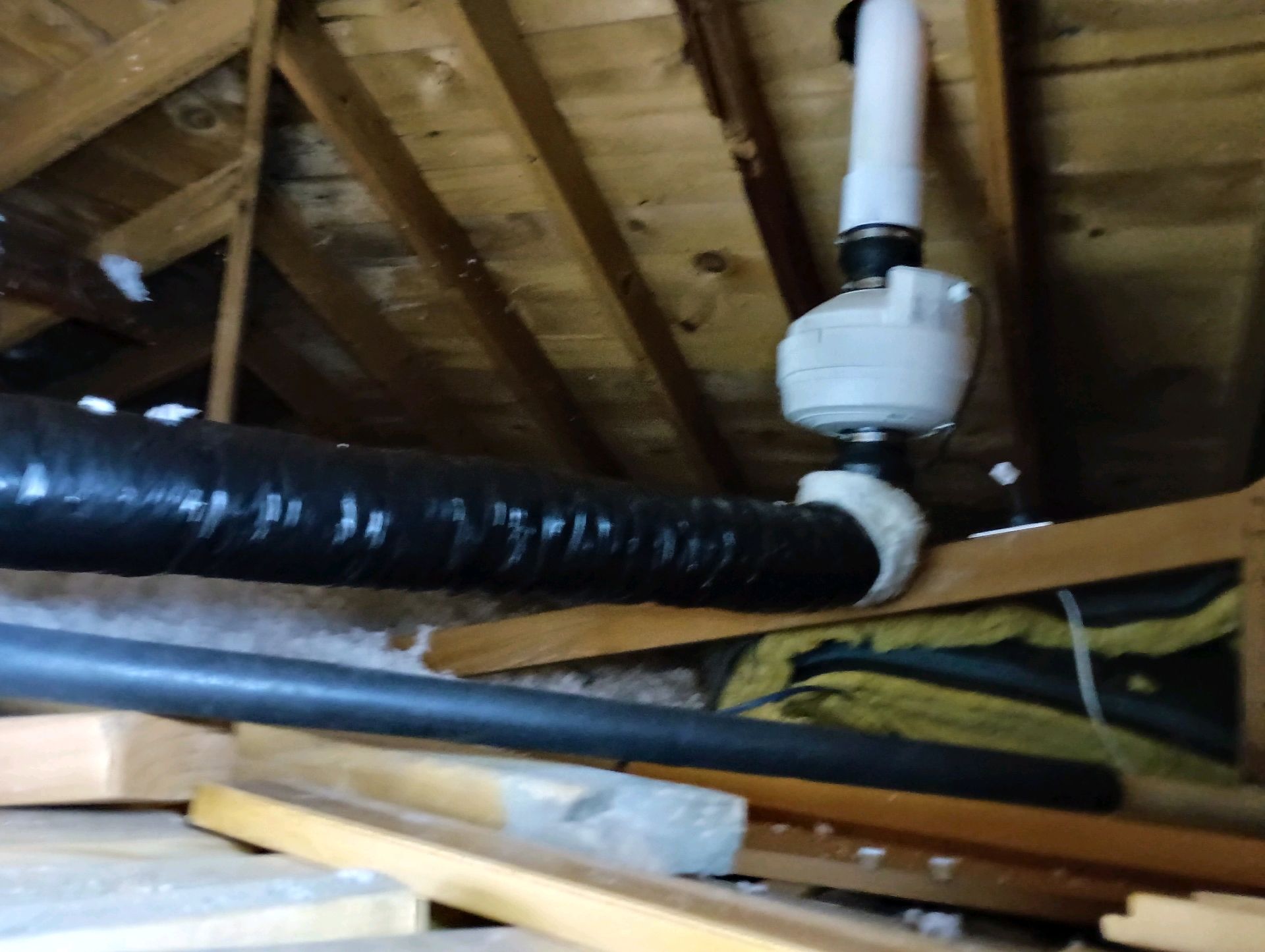 HVAC system components in an attic: flexible ductwork, a fan unit, and wood framing.