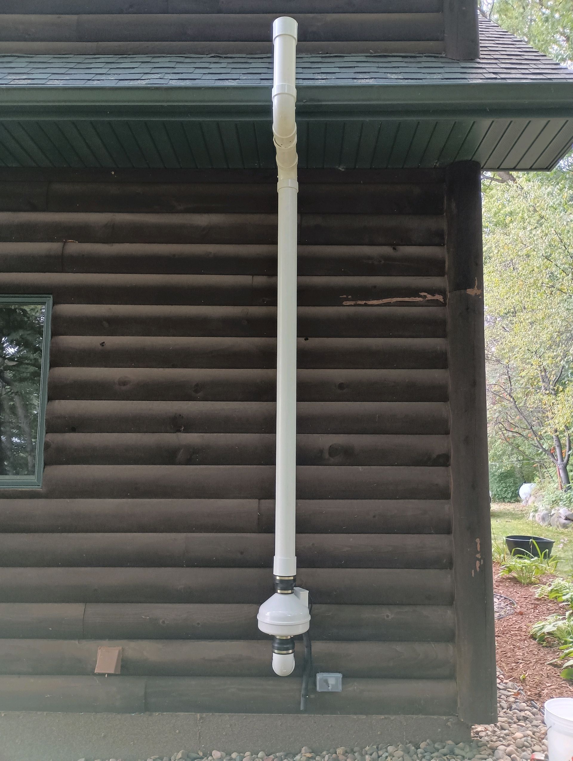 White PVC pipe vent on the side of a log cabin.