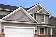 A gray house with a white garage door and a black roof.