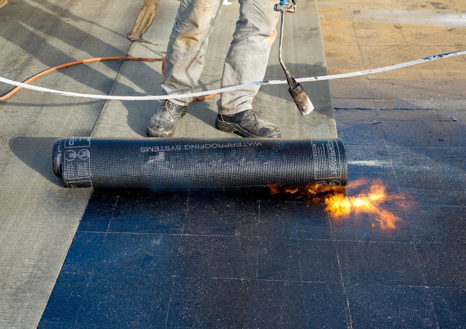 A residential roofing contractor preparing part of bitumen roofing for melting by a torch flame.