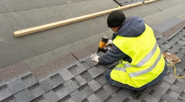 A man in a yellow vest is working on a roof.