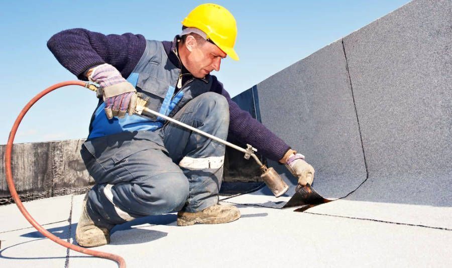 A man wearing a hard hat is working on a roof with a torch. A man wearing a hard hat is working on a roof with a torch.