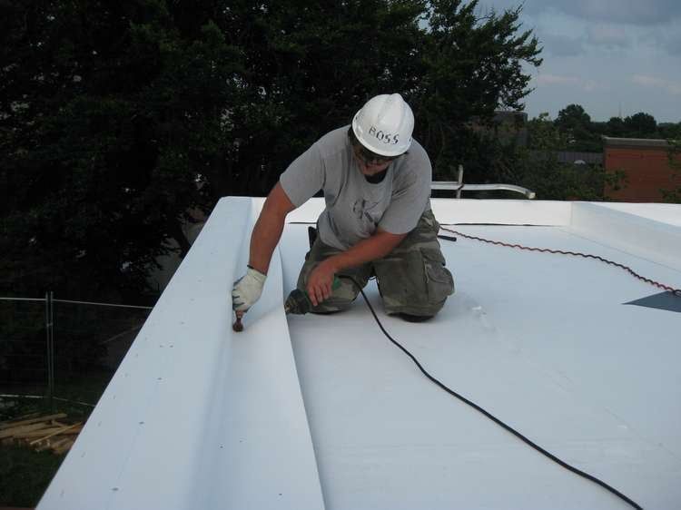 A man wearing a hard hat is working on a white roof