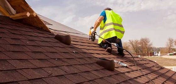 A man in a yellow vest is working on a roof.