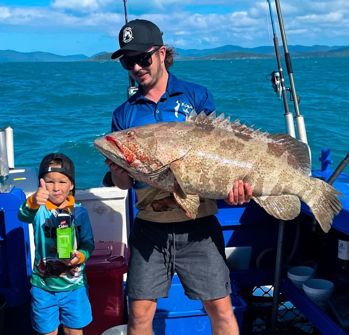 Man and a Boy Are Standing on a Boat Holding a Large Fish — Whitsunday Fishing Charters In Airlie Beach, QLD
