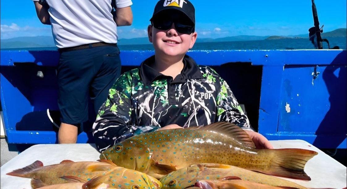 A Young Boy is Sitting on a Boat Holding a Large Fish — Whitsunday Fishing Charters In Airlie Beach, QLD