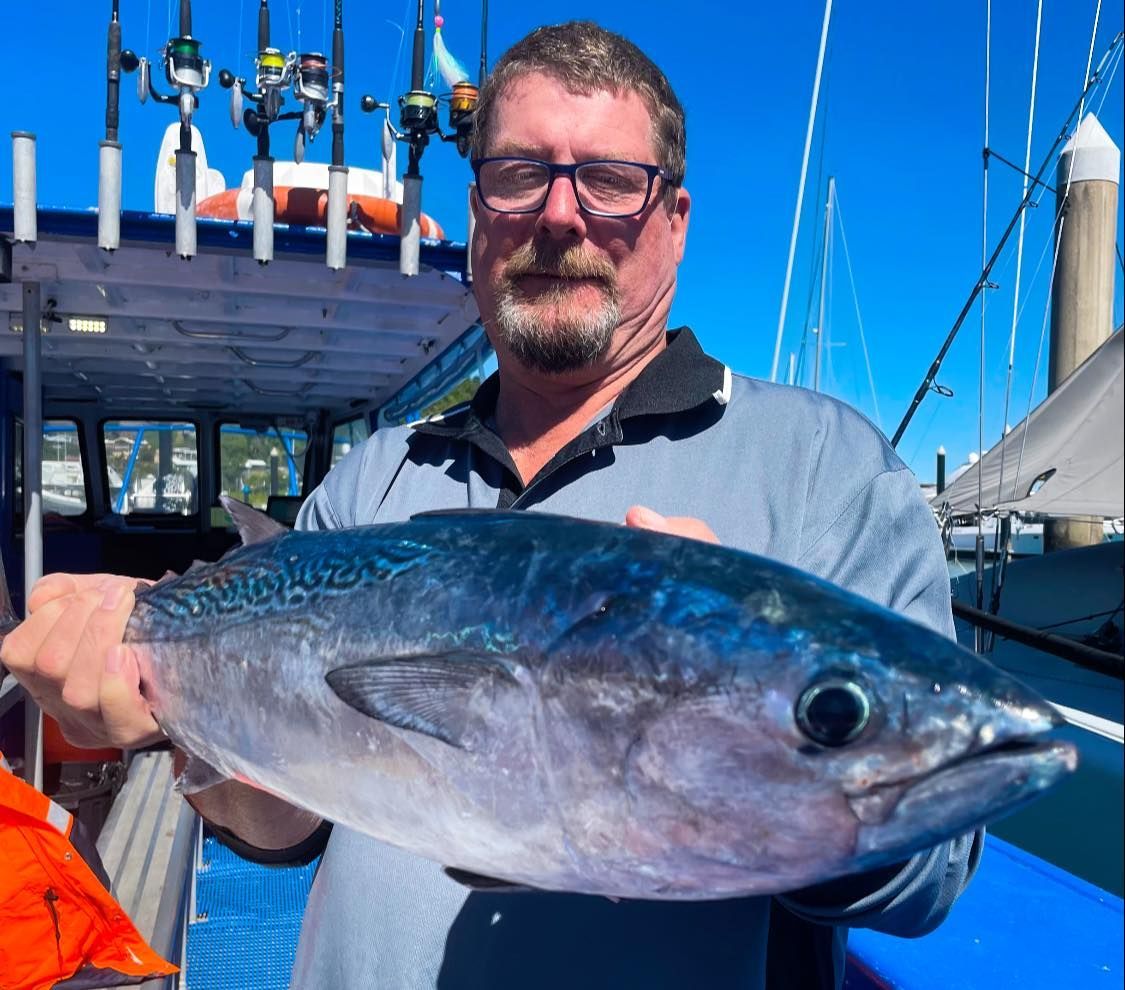 A Man is Holding a Large Fish in Front of a Boat — Whitsunday Fishing Charters In Airlie Beach, QLD
