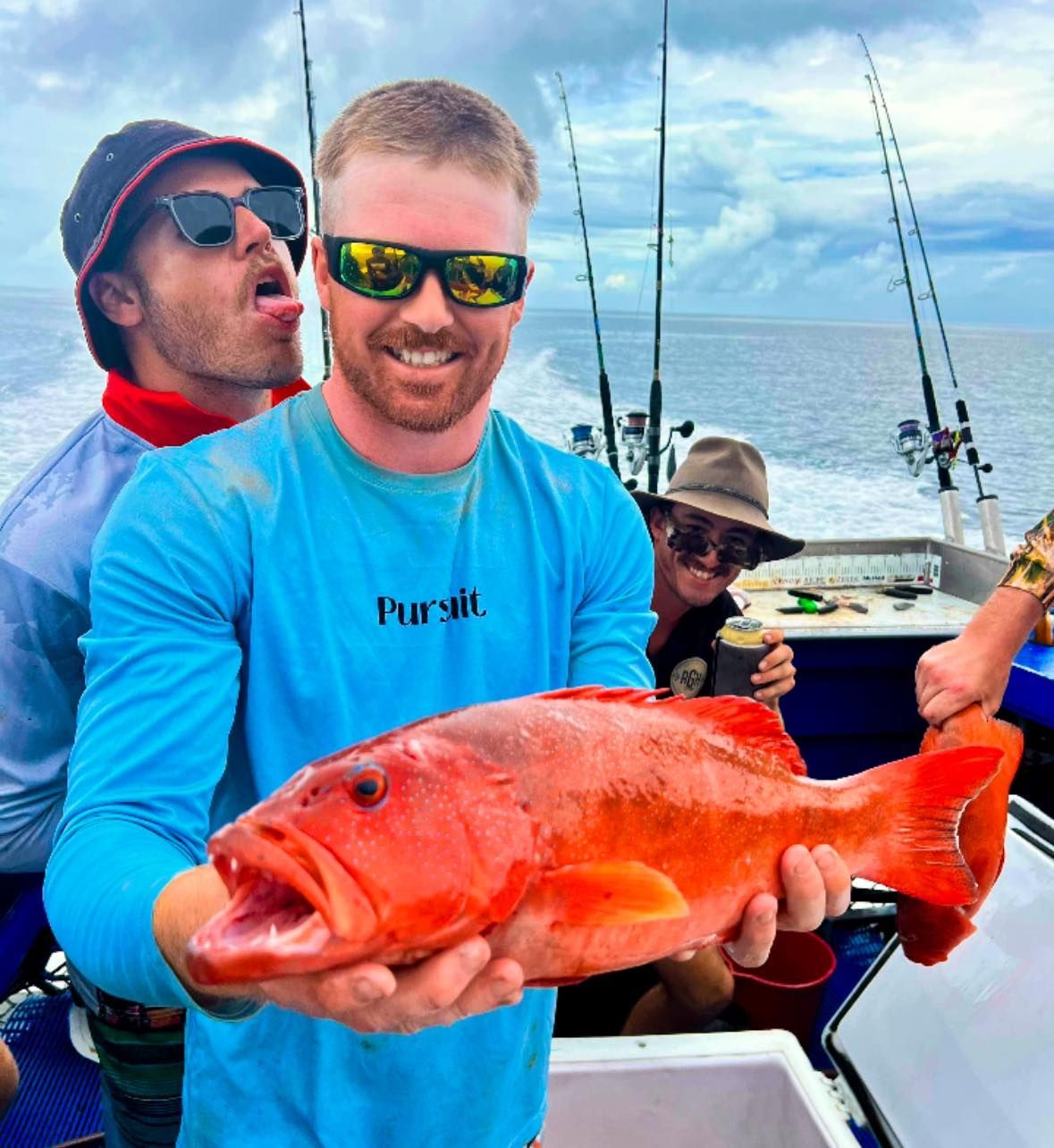 A Man Wearing a Blue Shirt That Says Pursuit is Holding a Red Fish — Whitsunday Fishing Charters In Airlie Beach, QLD