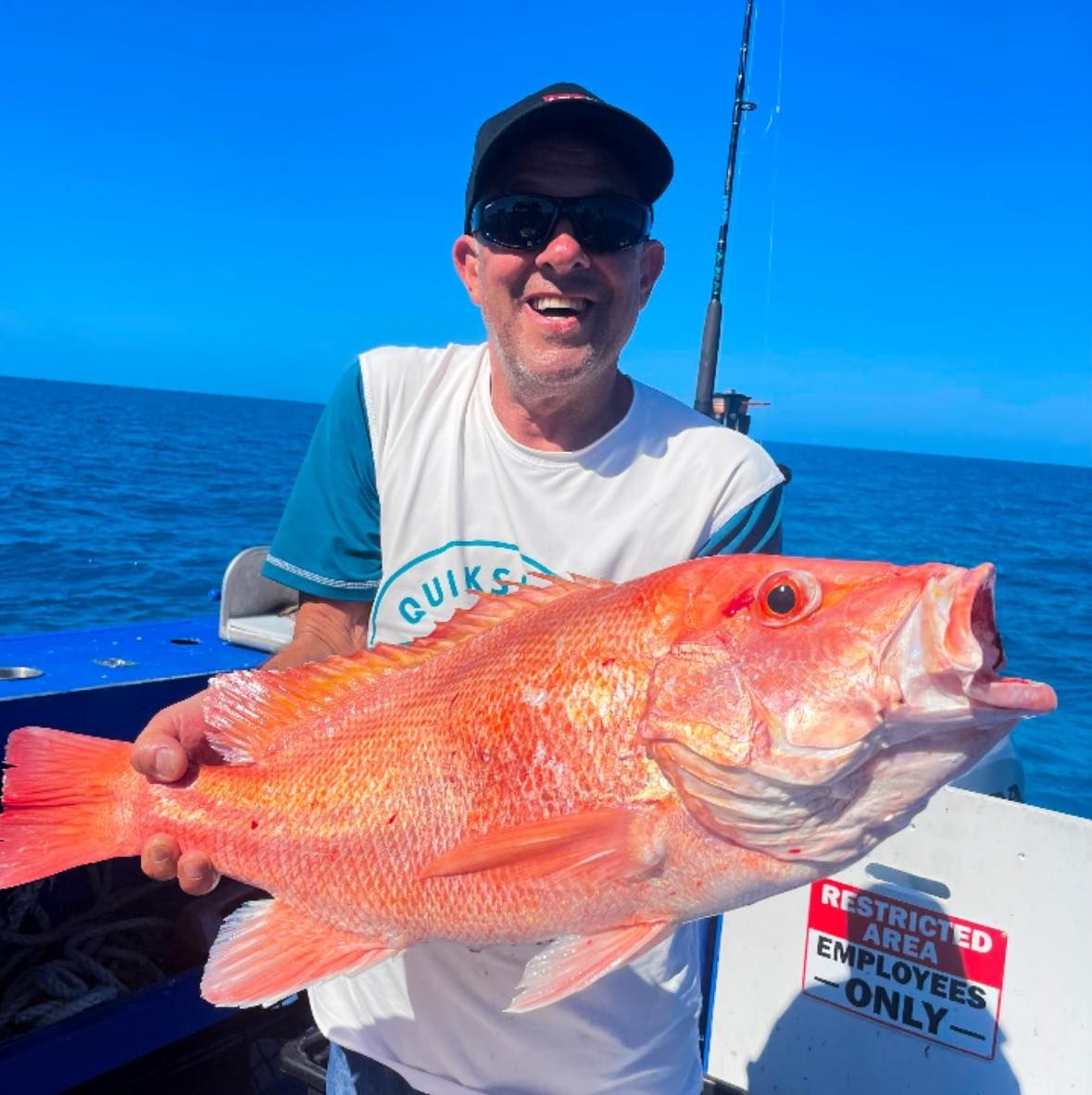 A Man is Holding a Large Fish in Front of a Sign — Whitsunday Fishing Charters In Airlie Beach, QLD