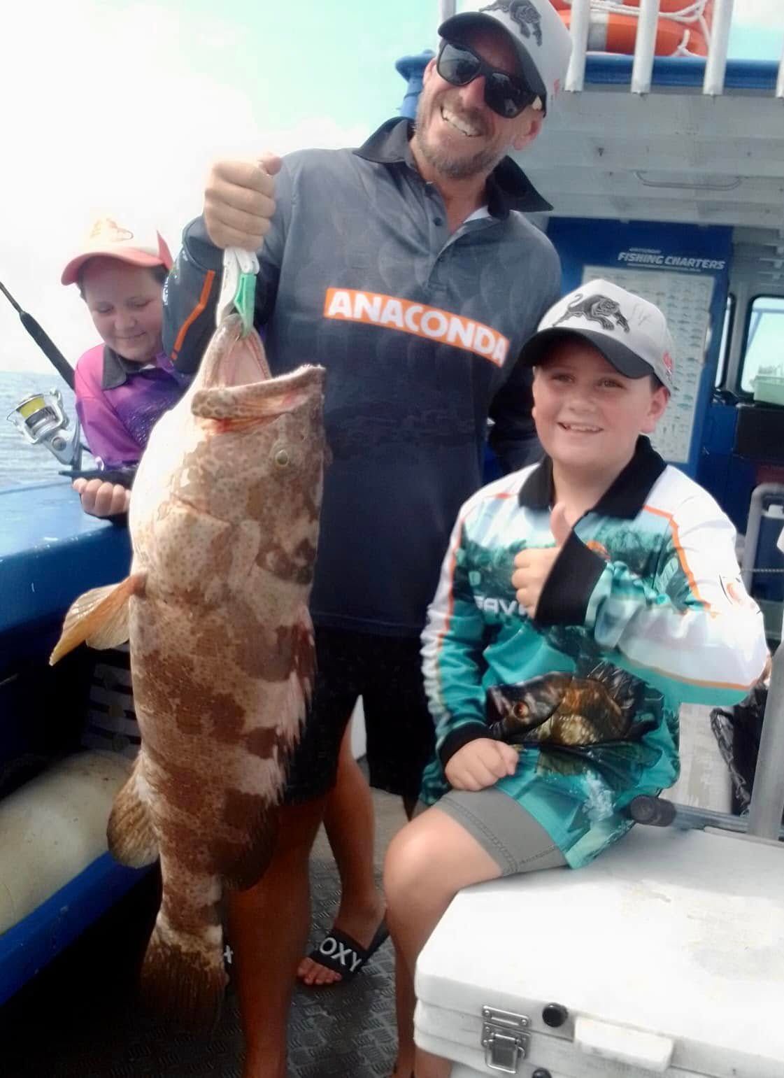 A Man and a Boy Are Holding a Large Fish on a Boat — Whitsunday Fishing Charters In Airlie Beach, QLD