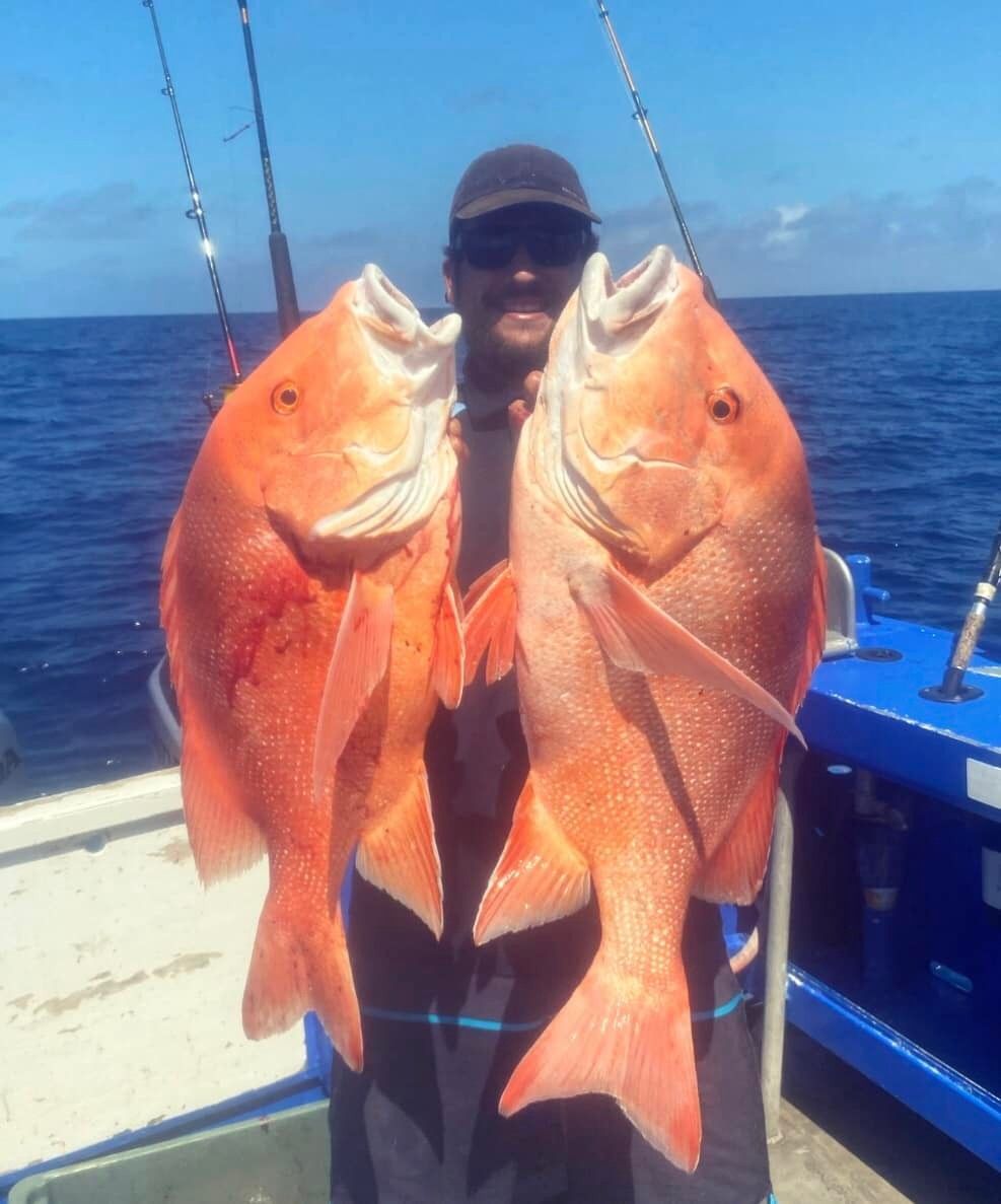 A Man is Holding Two Large Red Fish on a Boat — Whitsunday Fishing Charters In Airlie Beach, QLD