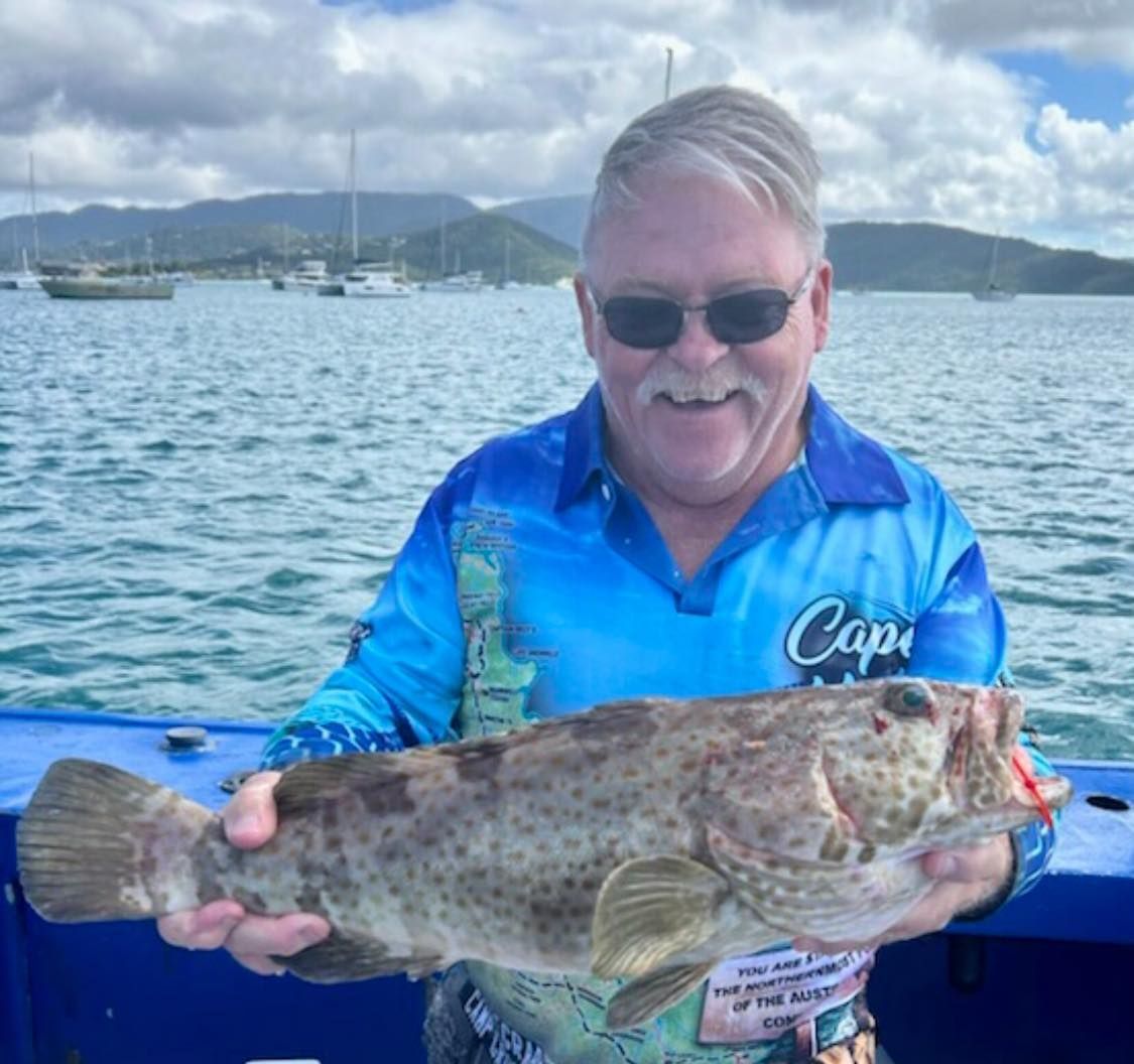 A Man in a Blue Shirt That Says Cape is Holding a Large Fish — Whitsunday Fishing Charters In Airlie Beach, QLD