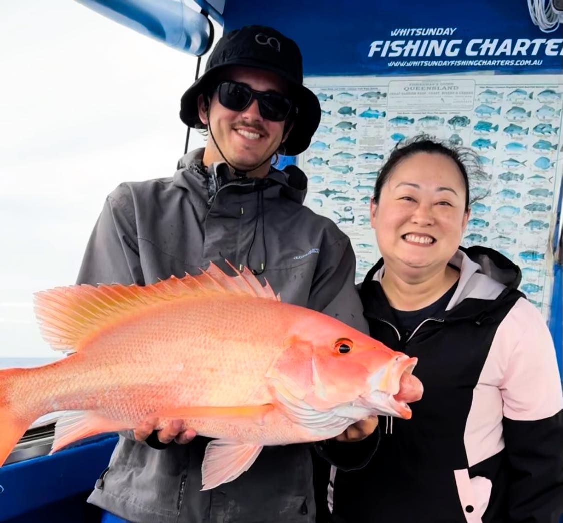 A Man and a Woman Holding a Large Fish in Front of a Fishing Chart — Whitsunday Fishing Charters In Airlie Beach, QLD