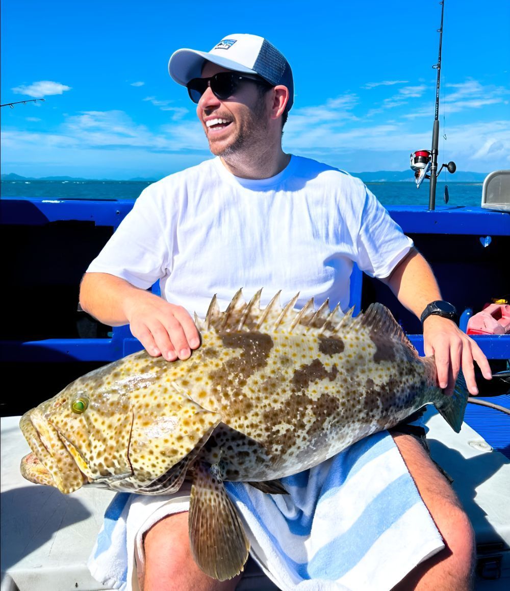 A Man is Sitting on a Boat Holding a Large Fish — Whitsunday Fishing Charters In Airlie Beach, QLD