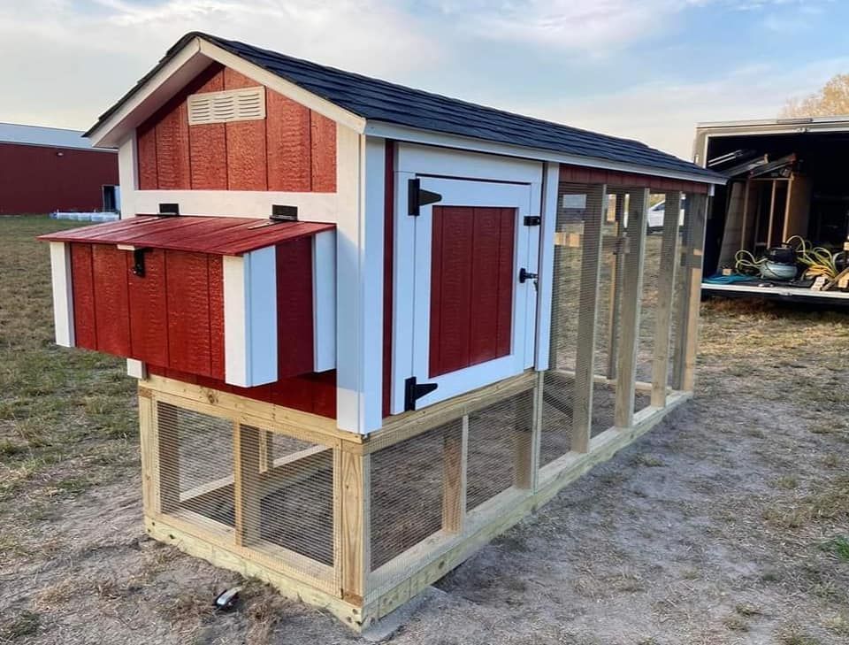 Red and white chicken coop with nesting box and wire run on a wood frame outdoors.