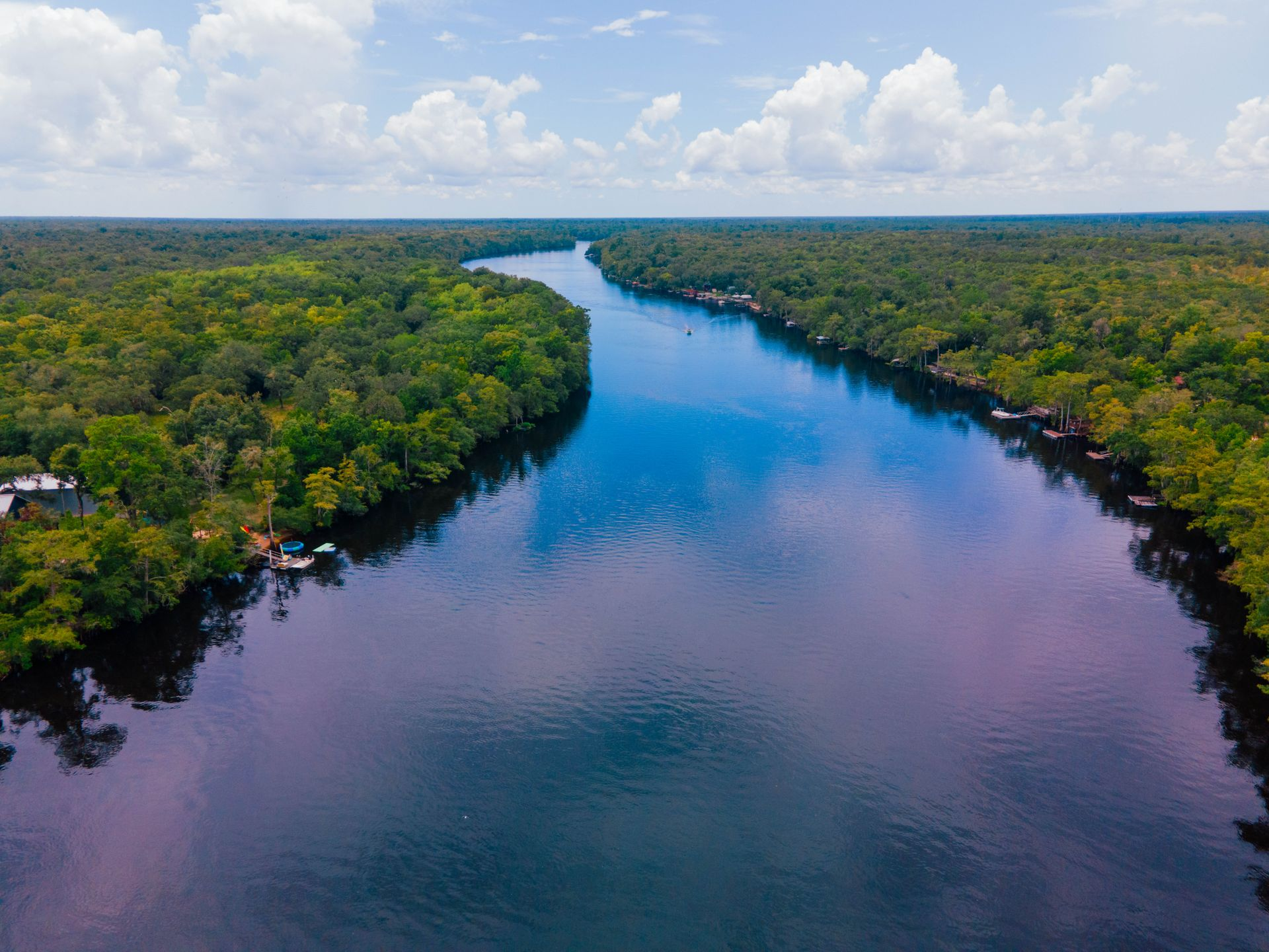 Aerial view of a wide blue river winding through dense green forest under a cloudy sky