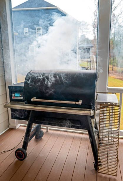 A black grill emits white smoke on a porch