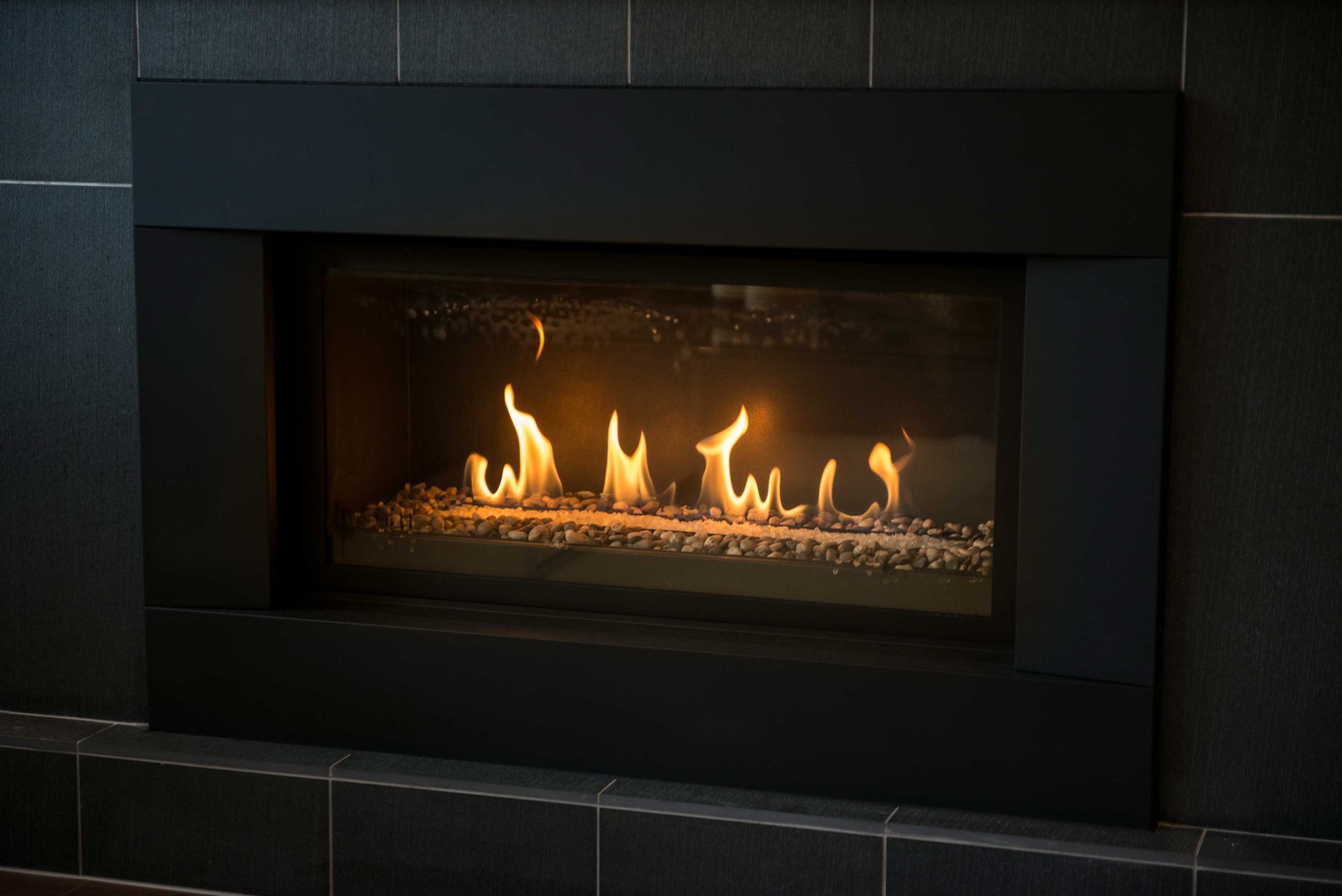 A fireplace with flames coming out of it is sitting on a tiled wall.