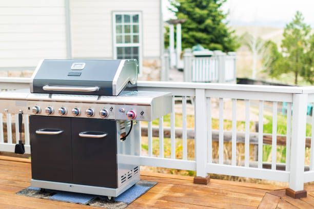 A grill is sitting on a wooden deck next to a white railing.